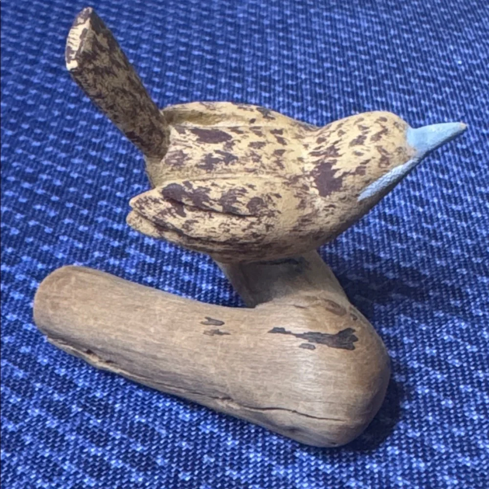 Hand carved wooden bird sculpture perched on a piece of natural wood signed